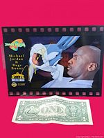 Front of the 1996 Space Jam movie cell card featuring Michael Jordan and Bugs Bunny with a gold signature of Michael Jordan. A dollar bill is placed underneath for size reference.