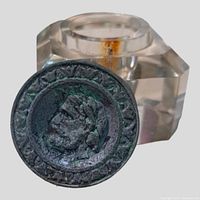 Close-up of metal lid showing Roman figure and laurel wreath detail with oxidation and patina.