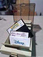 Front view of Tandy branded plastic storage box holding several 5.25-inch floppy disks with visible Disney Mickey Mouse and Beauty and the Beast labels.