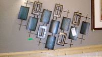 Full view of the metal wall art mounted on wall showing entire piece with all rectangular metal panels and frame.