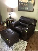 Front view of brown leather armchair with ottoman on wood floor