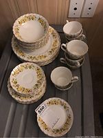 Top-down view of stacked plates, bowls, and several cups with floral yellow flower design around edges.