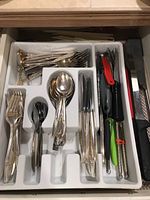 Drawer organized with Nobility silverplate forks, spoons, knives, and assorted kitchen utensils in a white tray