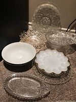 Overview of the lot showing eight serving dishes including milk glass deviled egg platter, ceramic bowls, and clear pressed glass platters and bowls.