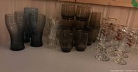 A set of 14 smoke coloured glasses in various sizes plus some clear stemmed grouse themed glasses on the right side of the photo with grouped bases