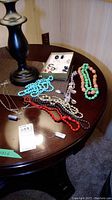 Overview photo of multiple beaded necklaces in turquoise, coral, black and white beads, silver chain necklace with round pendants, pierced earrings, and clip-on earrings on a wooden table.