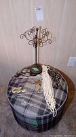 Overall photo showing the metal jewelry stand on a plaid round ottoman with assorted necklaces displayed around its base.