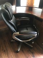Side profile of black leather Serta office chair showing padded armrests with metal frame, cushioned seat, and ergonomic backrest under desk corner