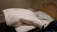 Bedding items including a white thick mattress topper folded on bed with light colored sheets