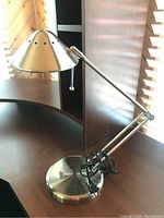 Photo of the full metal adjustable office table lamp showing the conical shade, adjustable arm, round base, and power cord with switch.