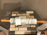 Marble rolling pin with wooden handles displayed horizontally on a decorative brick-pattern stand made of tile and stone.