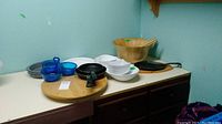 Full lot view showing a 15 inch wood lazy Susan, pans, blue and gray bowls, white ceramic pans and serving dishes, and cast iron grill pan with wood tray.