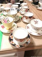 Photo showing five tea cups and saucers with various floral designs on table and lot tag