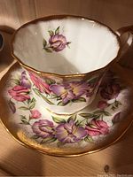 Close-up of tea cup with pink and purple floral pattern and gold trim on rim and handle