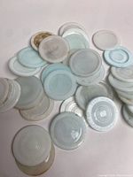 Group of 36 white and light blue milk glass mason jar lids showing their round shape and varying surface conditions.