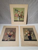 Three floral print plates displayed: top one mounted on board with a green background vase, bottom left with ornate urn and pink/white flowers, bottom right with dark blue vase and mixed flowers.