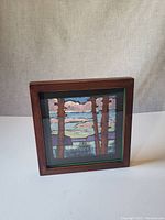 Front angled view of the signed painting in shadow-box frame showing the artwork of trees, lake and mountains.