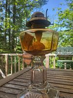 Full view of antique oil burning lamp showing amber glass reservoir and clear glass pedestal base, with metal burner and fabric wicks inside.