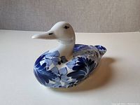 Side angle of the ceramic duck showing blue floral patterns and smooth white ceramic surface.
