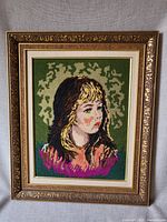 Framed vintage rug hook of a girl's portrait against a green background
