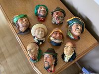 Nine colorful Bosson chalkware head figurines arranged on a wooden surface showing a variety of characters with hooks for hanging. All figurines display some wear and small chips.