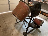 Side view of mixer showing red drum, gear ring, black frame and wheels
