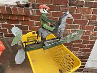 Side view of the early folk art whirly jig showing the painted rider on horse mounted on a green wooden base with metal propeller blades at rear.