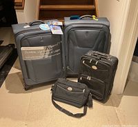 Photo showing two medium blue Travelpro Maxlite 2 luggage pieces along with an American Tourister black fabric carry-on and matching shoulder bag.