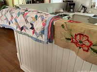 Both quilt and embroidered seat cover draped over railing in kitchen