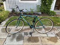 Teal Ramsays Nutra Giant 9-speed bicycle parked on a patio with a house siding and garden visible in background. Shows frame, tires, saddle, and handlebar.