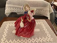 Front view of the figurine showing woman in red billowy dress, pale hat with blue bow, holding a muff.