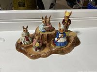 Front view of five Bunnykins figurines arranged on the tree stump display stand showing detailed clothing and poses.