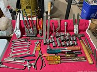 Overview of wrenches, pliers, vise grips, screwdrivers, hammer, punches, wire cutters, and files arranged on a red cloth.