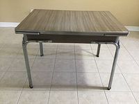 Front view of vintage kitchen table with variegated taupe Formica top and chrome legs in closed position.