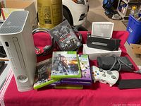 Front view of white Xbox 360 console, games, controller, cables, and accessories on red cloth