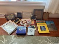 Overview of assorted picture frames, several gardening and houseplant books, and decorative tins arranged on wooden floor near window