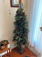 Full view of the 59-inch tall faux Christmas tree in a metal stand, decorated with pinecones and red berries.
