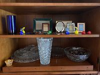 Shelf display of assorted decorative glass pieces, multiple picture frames, and colorful glass candy figurines