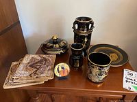 Full set of Greek porcelain items displayed on wooden surface including vases, plates, coasters, and cup.