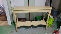 Front view of cream painted wood hall table showing turned legs and scalloped lower shelf.