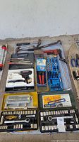Overview of various hand tools including socket sets, tap and die set, soldering tool, pliers, files, and hammers arranged on floor