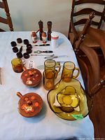 Full lot overview showing amber glass bowls, mugs, wood napkin rings, salt shaker, pepper grinder, cutlery and table linens on a white table.