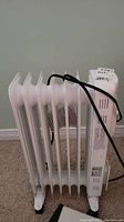 Side view of white oil-filled wheeled stand heater with power cord wrapped around it.