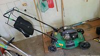 Full view of the green Certified lawnmower with attached grass collection bag and black engine cover, wheels, and handle.