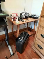 Full view of lot items on wooden table and floor, showing walkie-talkie box, Alcatel phone, Craig CD player radio, and Sylvania shredder