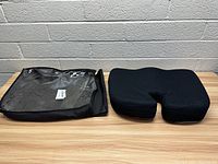 Photo of the black seat cushion and its carrying case side by side on a wooden table against a brick wall.