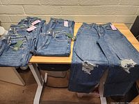 Six pairs of women's jeans laid out on a wooden table, showing overall condition and different styles.