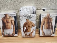 Three packages of Calvin Klein men's underwear on display. Two 3-packs of cotton stretch briefs and one pack with 100% cotton briefs in white color.