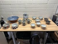 Wide shot of assorted stoneware dishes including bowls, mugs, and pitcher on wooden table