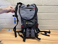 Gray and black Outdoor Products hydration pack with blue hydration bite valve and adjustable straps.